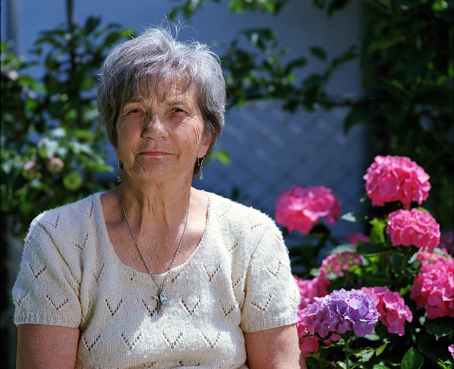 Elderly woman sitting in front of rose bush