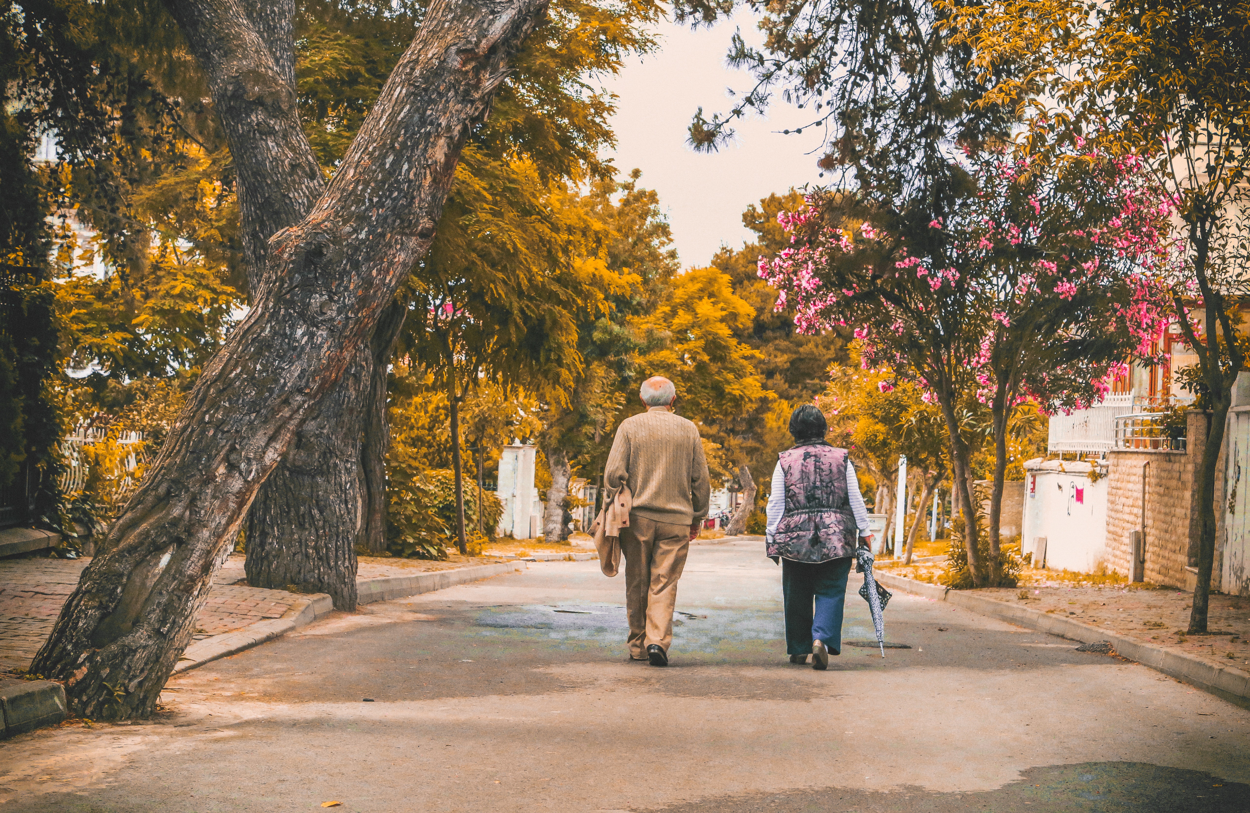 Elderly man & woman walking down tree-lined street. Photo by Emre Kuzu from Pexels