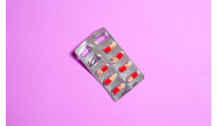 package of red and yellow pills on a pink background