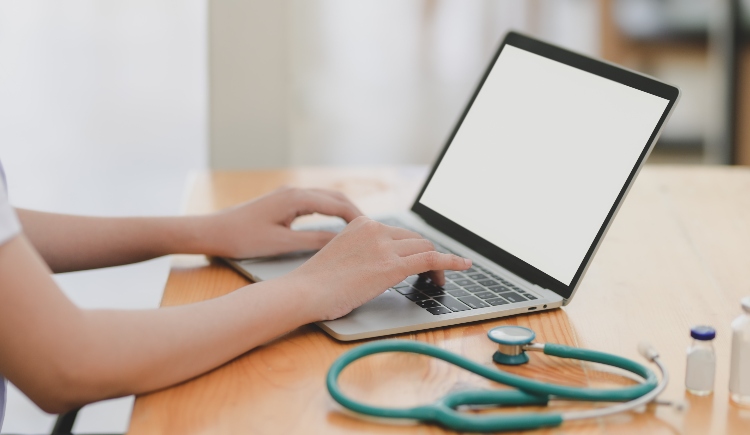 Person on laptop next to stethoscope Photo by bongkarn thanyakij from Pexels
