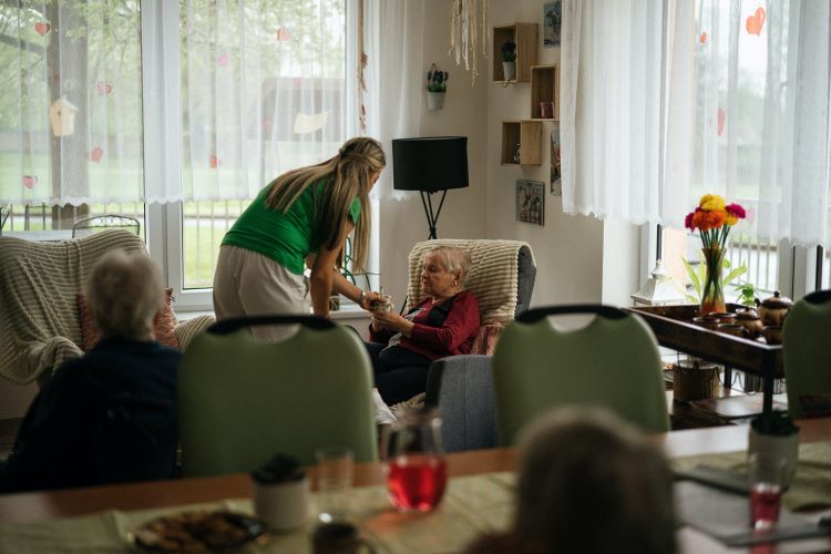 nurse attends to seated patient in a community room at nursing facility