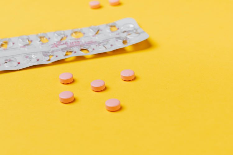 silver pill pack and orange pills on golden yellow background