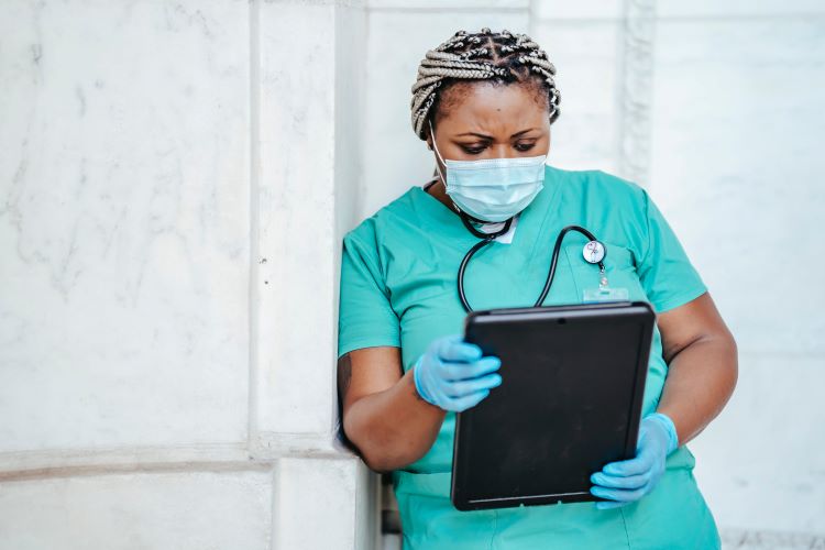 nurse standing in turquoise scrubs and face maks, reading tablet