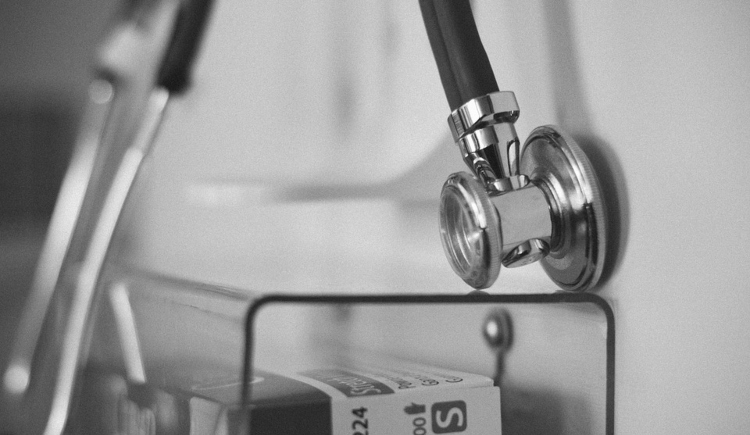 Black and white photo of stethoscope hanging on wall over shelf