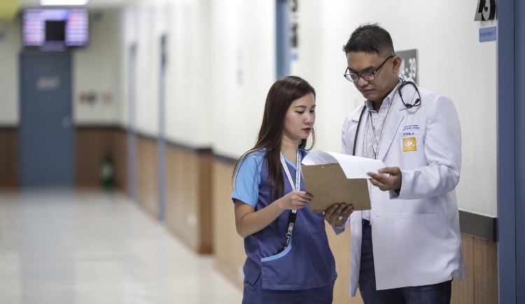 Nurse and doctor standing in hallway looking at clipboard