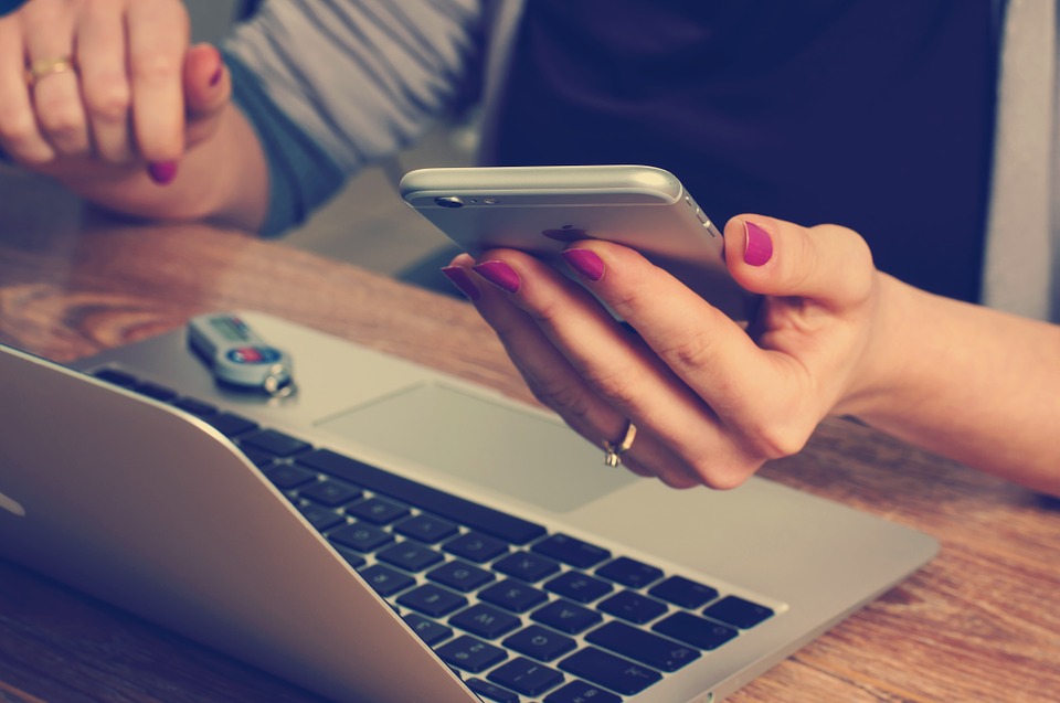 Woman's hand holding cell phone in front of computer