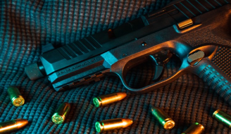 handgun and bullets on dark grey surface under blue light