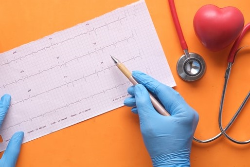 blue gloved hands with yellow pencil examine chart on orange table with red stethoscope and heart